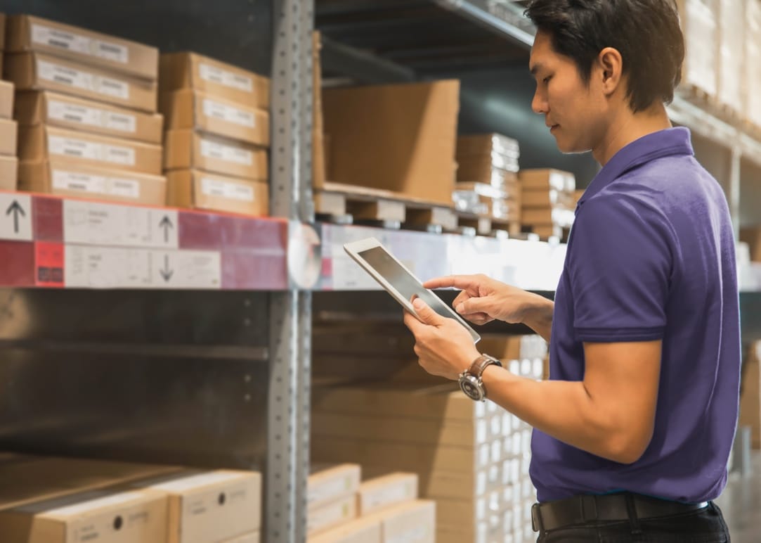 Photo of a warehouse worker holding a tablet device in an aisle with tall shelving